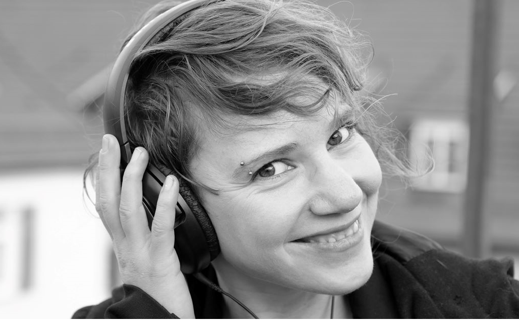 Mirjam Karrer Profilfoto in schwarz-weiß mit Kopfhörern. Die junge Frau hat eine Kurzhaarfrisur und lächelt freundlich auf dem Foto